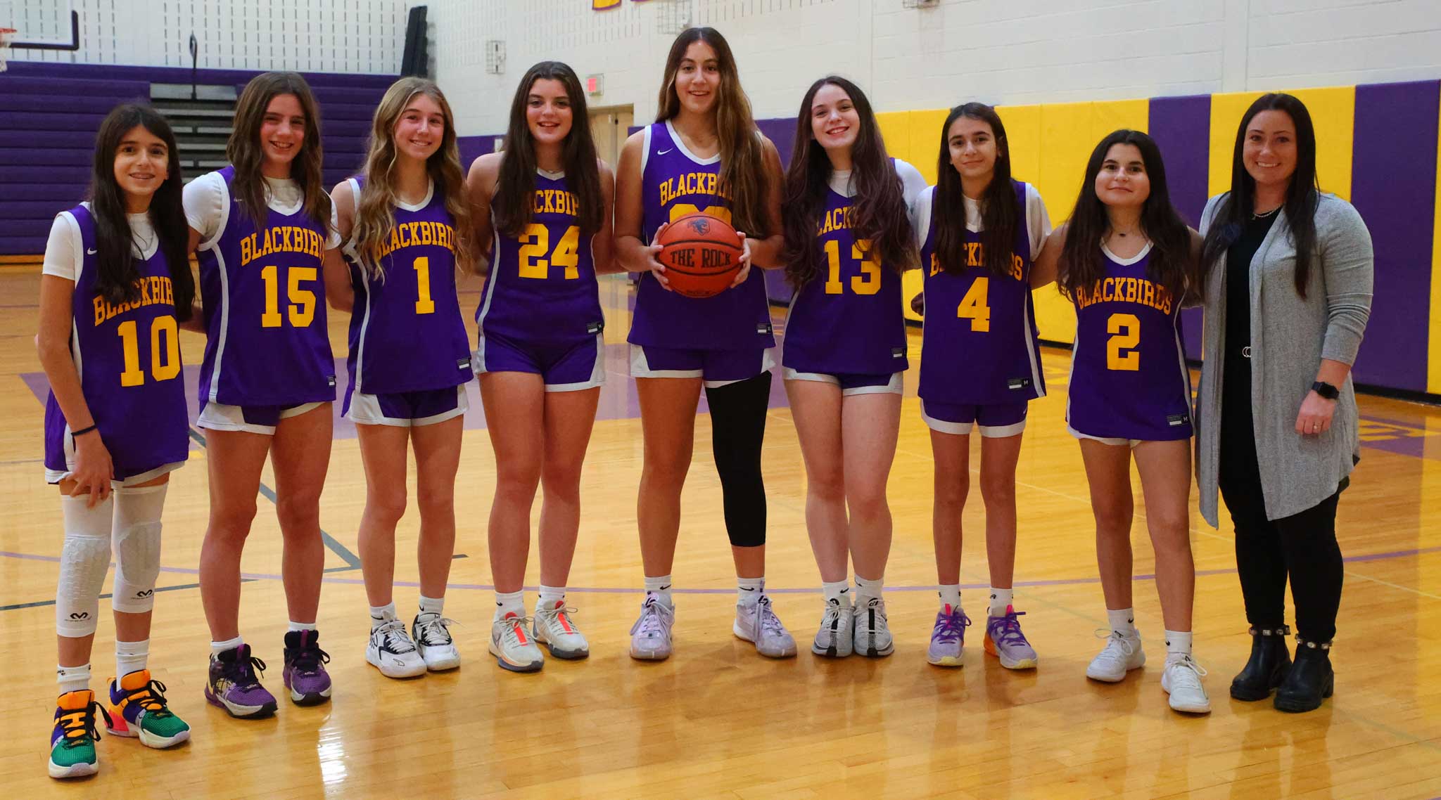 Voorheesville basketball team with blackbirds jerseys on. Coach is in group photo. Center player holds basketball.