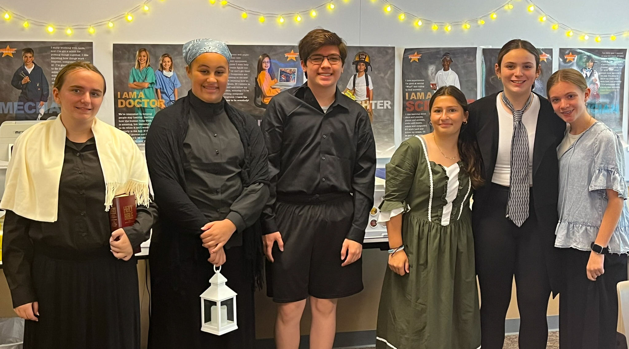 Six middle school students dressed as historical figures. One is holding a bible; another is holding a lantern.