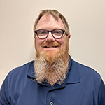 VCSD Board of Education member, Matthew Bergeron, who has short reddish blond hair and long beard and wears dark rimmed eyeglasses, looks at and smiles for the camera.