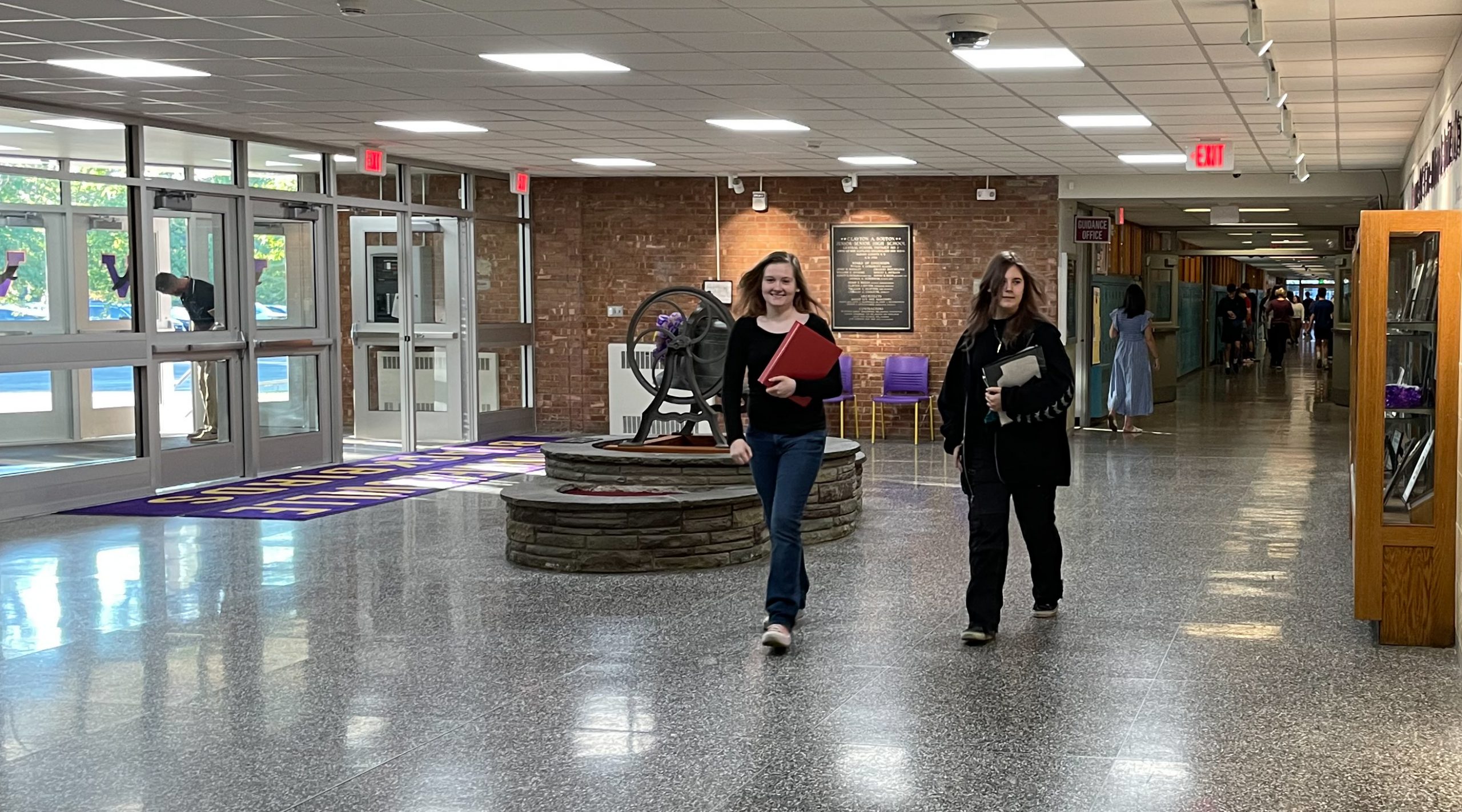 Two students walk in Voorheesville vestibule. Additional students in background in hallway.