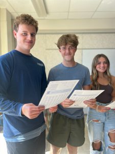 Three students stand in classroom. They are each holding a voter pre-registration form.