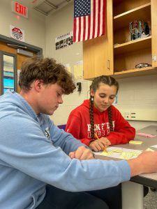 Two high school students at desk with paper.