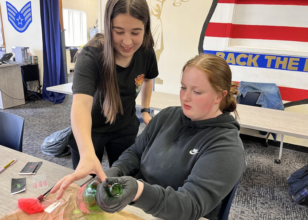 Alexzina Merritt and Rayah McCallus practice dusting for fingerprints using a bottle.