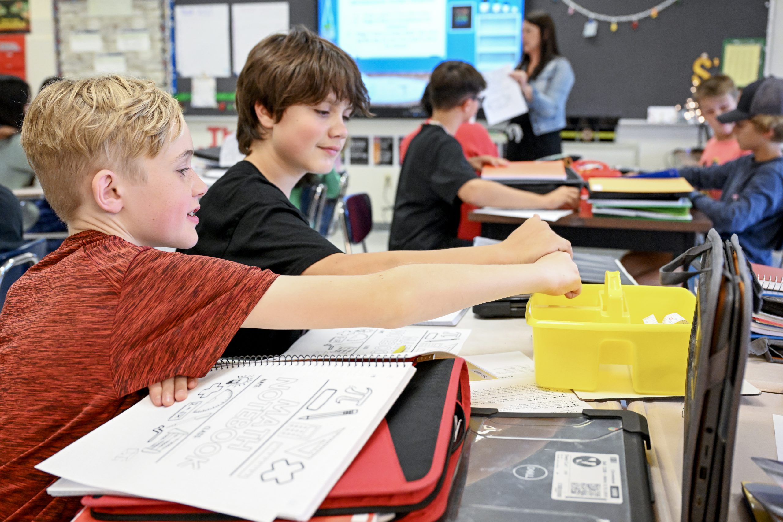 Students working side-by-side at desks in middle school Teacher in background.