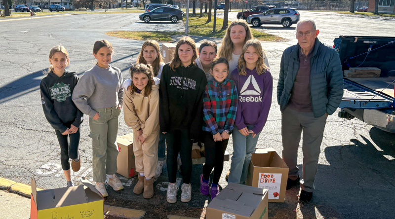 Nine students and one adult standing in parking lot with food drive boxes.