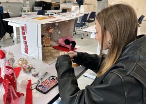 Teen creates a miniature window display of fashions with a December holiday theme.