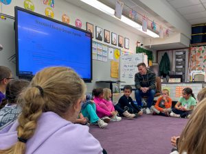 Teacher talks to students gathered in a circle.