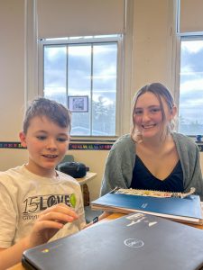 Grade five student sits next to a teen at a desk.