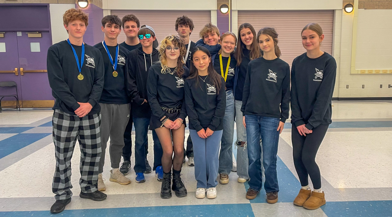 Twelve students wearing matching shirts stand in a group. Four have medals around their necks.